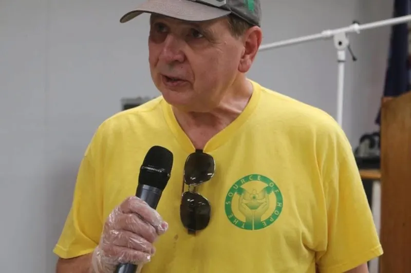 A Source of Hope volunteer in a food-service glove speaking into a microphone