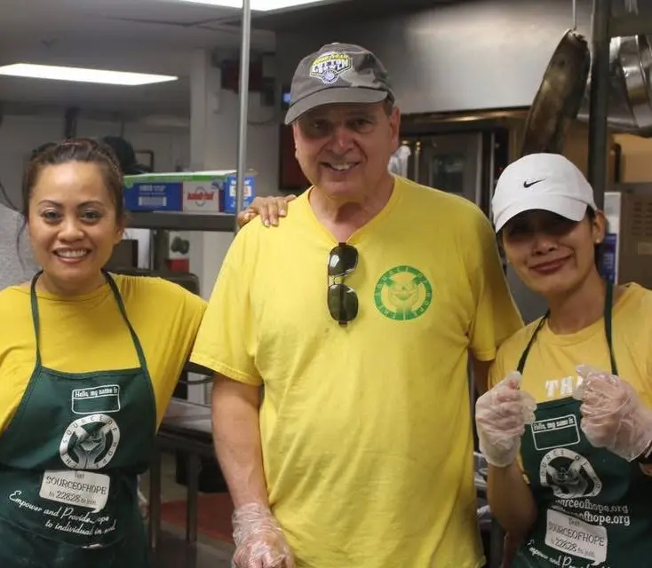 Three Source of Hope volunteers in aprons and gloves smiling together in a kitchen
